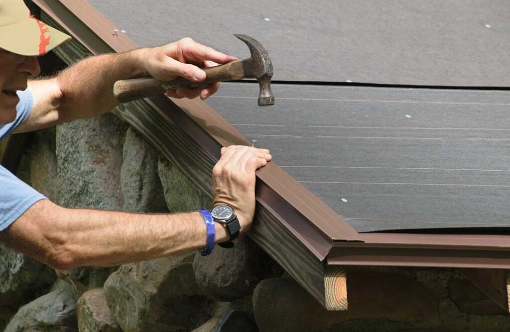 A worker installs new shingles on a sloped residential roof under bright daylight.